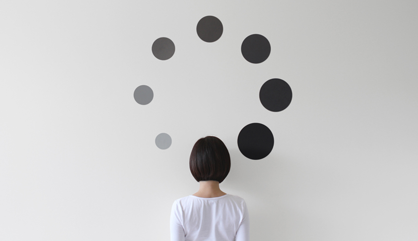 A woman facing wall surrounded by black spots